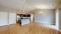Located at 48 Bavarian Way in Altamont, NY, this well-appointed 2-bedroom, 2-bathroom single-story home offers a thoughtfully designed layout with modern finishes throughout. The heart of the home is an open-concept kitchen and living area highlighted by soaring vaulted ceilings, pendant lighting, and a elegant chandelier. The kitchen features rich dark wood cabinetry, granite countertops, stainless steel appliances, a tile backsplash, and a central island with a sink — ideal for both everyday living and entertaining. Warm hardwood-style flooring flows seamlessly throughout the main living areas, complemented by neutral gray walls and abundant natural light from large windows and a sliding glass door. The spacious primary bedroom includes a ceiling fan, multiple windows with natural light, and generous closet space — one of three closets found throughout the home. Both bathrooms are finished with granite-topped dark wood vanities and tile flooring; one features a walk-in shower while the other includes a tub/shower combination. Additional spaces include a dedicated laundry room, a pantry, and a hallway connecting the private quarters. The overall ambiance is clean, modern, and move-in ready.
