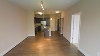 This single-floor residence showcases an open-concept layout that seamlessly connects the living area to the kitchen, creating a spacious and functional flow. Rich, dark hardwood flooring extends throughout the main living space, adding warmth and a cohesive aesthetic.

The kitchen is a standout feature, equipped with dark espresso cabinetry that provides ample storage, stainless steel appliances including a French door refrigerator with an ice and water dispenser, and a built-in range. A central island with a light-toned countertop and an undermount sink serves as both a functional workspace and a natural gathering point. Pendant lighting hangs above the island, complementing the flush-mounted ceiling lights that illuminate the space.

The open living area benefits from a neutral color palette on the walls, allowing the dark flooring and cabinetry to take center stage. A corridor visible beyond the kitchen hints at additional rooms, including what appears to be a laundry area. A doorway to the right of the main space leads to a separate room, adding to the overall functional layout. The design balances contemporary style with everyday practicality.