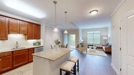 Located at 1 Millers Way in Simsbury, Connecticut, this well-appointed two-bedroom, two-bathroom residence offers a thoughtfully designed single-floor layout. The open-concept kitchen is a standout feature, showcasing rich cherry wood cabinetry, granite countertops, a center island with bar seating, and a full suite of stainless steel appliances including a refrigerator, range, microwave, and dishwasher. A tile backsplash and pendant lighting complete the space, while in-unit washer and dryer hookups add everyday convenience. The kitchen flows seamlessly into the dining area and the bright, welcoming living room, which features wood-style flooring, crown molding, and large windows alongside a sliding glass door that opens to an outdoor balcony, filling the space with natural light and views of lush greenery. The spacious primary bedroom is carpeted and benefits from multiple windows, while the second bedroom is equally comfortable with soft carpet and natural light. Both bathrooms are finished with granite vanities and tile flooring; the primary bath includes a glass-enclosed shower. A hallway and dedicated closet provide additional storage throughout this well-rounded, move-in-ready home.