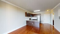 Located at 814 N Third St in Wilmington, NC, this single-floor unit offers a well-designed layout with consistent hardwood flooring throughout. The open-concept living and kitchen area serves as the heart of the space, featuring a peninsula with granite countertops that provides both workspace and a natural divider between the living area and the kitchen. The kitchen is equipped with rich, dark-stained cabinetry, a decorative tile backsplash, and a full suite of stainless steel appliances including a refrigerator, electric range, and built-in microwave. Crown molding accents the living and kitchen area, adding a polished architectural touch. The bedroom is bright and inviting, benefiting from a large window that frames views of surrounding greenery and allows generous natural light to fill the room. A ceiling fan adds to the comfort of the space. A dedicated area provides a walk-in closet with wire shelving alongside a stacked washer and dryer unit, offering convenient in-unit laundry. The bathroom includes a full soaking tub and shower combination with clean white surroundings and granite-accented vanity surfaces. Neutral wall tones throughout create a calm, cohesive atmosphere well-suited to a variety of furnishing styles.