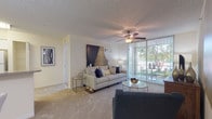 This single-story residence offers a thoughtfully arranged layout with distinct living, dining, kitchen, bedroom, and bathroom areas. The living room serves as the central gathering space, featuring wall-to-wall carpet, a textured ceiling, and a ceiling fan with integrated lighting. A large sliding glass door lined with vertical blinds allows abundant natural light to fill the room and provides direct access to an outdoor balcony, where views of surrounding greenery are visible. The dining area is positioned near the entryway and accommodates a dining table, complemented by decorative wall art that adds a refined touch.

The kitchen is efficiently designed with white cabinetry extending to the ceiling, granite-style countertops, a stainless steel sink, and a full suite of white appliances including a refrigerator, electric range, and over-the-range microwave. Light tile flooring runs throughout the kitchen, contrasting with the carpeted living areas.

The bedroom is generously proportioned, featuring plush carpet, a ceiling fan, and a window with vertical blinds that invite natural light. Two full bathrooms serve the residence, each equipped with a tub-shower combination, white tile surround, granite-topped vanity, and tile flooring, offering a clean and functional design throughout.