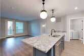 This well-appointed 2-bedroom, 2-bathroom residence in Columbus, Ohio offers a thoughtfully designed single-floor layout with modern finishes throughout. The open-concept kitchen and living area serves as the heart of the home, anchored by a striking navy blue island topped with granite countertops and illuminated by two statement globe pendant lights. White upper cabinetry, a decorative tile backsplash, stainless steel appliances, and light hardwood flooring complete the kitchen's polished, contemporary look. The living area flows seamlessly from the kitchen, bathed in natural light from large windows. The primary bedroom is generously sized, showcasing elegant wainscoting wall paneling with gold sconce lighting, plush carpeting, and access to a walk-in closet with built-in shelving. The second bedroom also features wainscoting detail and exterior door access. Both bathrooms are finished with marble-look tile flooring, granite vanity tops, and black hardware accents. A dedicated in-unit laundry room includes a full-size washer and dryer with overhead shelving. Two well-sized closets with multi-tier shelving provide ample storage. The space combines upscale design elements with practical functionality, creating a refined and comfortable living environment.