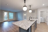This well-appointed 2-bedroom, 2-bathroom residence in Columbus, Ohio offers a thoughtfully designed single-floor layout with modern finishes throughout. The open-concept kitchen and living area serves as the heart of the home, anchored by a striking navy blue island topped with granite countertops and illuminated by two statement globe pendant lights. White upper cabinetry, a decorative tile backsplash, stainless steel appliances, and light hardwood flooring complete the kitchen's polished, contemporary look. The living area flows seamlessly from the kitchen, bathed in natural light from large windows. The primary bedroom is generously sized, showcasing elegant wainscoting wall paneling with gold sconce lighting, plush carpeting, and access to a walk-in closet with built-in shelving. The second bedroom also features wainscoting detail and exterior door access. Both bathrooms are finished with marble-look tile flooring, granite vanity tops, and black hardware accents. A dedicated in-unit laundry room includes a full-size washer and dryer with overhead shelving. Two well-sized closets with multi-tier shelving provide ample storage. The space combines upscale design elements with practical functionality, creating a refined and comfortable living environment.
