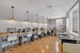Located at 36125 Creighton Ave in Murrieta, California, this single-floor professional office space is thoughtfully designed to support a productive work environment. The main open area features a long built-in granite-topped workstation along one wall, outfitted with multiple desktop computers and ergonomic rolling chairs, all illuminated by a series of stylish industrial pendant lights suspended from the ceiling. Textured accent wallpaper adds visual interest behind the workstation, complementing the warm-toned hardwood flooring that runs throughout. A dedicated private office nook includes built-in cabinetry with file drawers, a wrap-around desk surface, and a window that brings in natural light — ideal for focused, individual work. A lounge seating area with contemporary armchairs and low side tables provides a comfortable space for informal meetings or waiting. A separate enclosed conference room serves as the formal meeting space, featuring a large rectangular wood table, upholstered seating, a wall-mounted flat-screen display, and multiple windows fitted with blinds that allow for controlled natural light. The overall design palette of soft grays, warm wood tones, and neutral furnishings creates a clean, modern, and professional ambiance throughout.