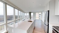 This contemporary 3-bedroom, 3-bathroom residence offers a seamless blend of modern design and urban living. The open-concept layout is anchored by a sleek, modern kitchen featuring an expansive quartz island with an integrated sink, flat-front cabinetry, and stainless steel appliances. Light hardwood flooring flows throughout the space, complementing the clean, neutral color palette. One of the most striking features of this residence is the dramatic floor-to-ceiling window system that spans the main living area, flooding the interior with abundant natural light and framing panoramic views of the surrounding cityscape. A structural concrete column adds an industrial accent that contrasts elegantly with the refined finishes throughout. The open living and dining areas benefit directly from the wall of glass, creating an airy, elevated atmosphere with a strong connection to the outdoors. The three bedrooms and three full bathrooms provide generous accommodation, making this an ideal space for comfortable everyday living. The overall ambiance is bright, sophisticated, and modern, with thoughtful architectural details that enhance both function and aesthetic appeal throughout.