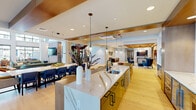 The James Run Apartments clubhouse is a thoughtfully designed community amenity space spanning a generous single floor. Guests are welcomed by a polished reception lobby featuring large-format stone tile flooring, a textured stone accent wall, bold navy and warm wood paneling, and a professional front desk — setting a refined, contemporary tone throughout.

The open-concept social hub at the heart of the space features a striking kitchen island finished in gold cabinetry and topped with dramatic veined quartz countertops. Sleek pendant lighting cascades above, while an adjoining dining area with navy upholstered seating comfortably accommodates a large group. The kitchen flows seamlessly into multiple lounge zones furnished with a curated mix of teal, cobalt, and cognac leather seating atop patterned area rugs, all grounded by wide-plank light hardwood flooring.

Soaring double-height ceilings and floor-to-ceiling black-framed windows define the main living lounge, flooding the space with abundant natural light and offering open views to the outdoor community. Globe pendant lights add an airy, sculptural quality overhead.

A dedicated game room provides a change of pace, centered around a full-size billiards table beneath a circular pendant fixture. Built-in bar-height seating, a large-screen TV, and intimate wood-paneled booth nooks complete the entertainment experience.