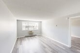 Located at 8 Old Colony Ln in Arlington, MA, this one-bedroom, one-bathroom residence offers a thoughtfully laid-out single-floor plan with a clean, modern aesthetic throughout. Light-toned luxury vinyl plank flooring flows consistently across all rooms, complemented by neutral gray walls, crisp white trim, and textured ceilings that give the space a fresh, well-maintained feel.

The living room is the largest area in the home, offering generous proportions and natural light through a wide window overlooking greenery outside. A wall-mounted air conditioning unit and baseboard heating provide year-round climate control. The open, airy feel makes it well-suited for a variety of furniture arrangements.

The kitchen features white cabinetry with ample upper and lower storage, a stainless-style sink, white appliances including a range and dishwasher, and matching light flooring that ties the space together cohesively.

The spacious primary bedroom includes a window for natural light, baseboard heating, and two closets with bifold doors. In total, the residence offers five closets, providing exceptional storage throughout.

The bathroom includes a full tub-shower combination with warm-toned tile accents and a vanity with mirror. The overall layout is efficient and functional, making excellent use of every square foot in this well-appointed Arlington residence.