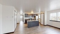 This single-floor residence offers a clean, modern layout designed for comfortable everyday living. The heart of the home is an open-concept kitchen, anchored by a center island with an undermount sink and ample counter space finished in neutral tones. Dark espresso cabinetry lines the walls, providing generous storage, while stainless steel appliances — including a range, built-in microwave, refrigerator, and dishwasher — lend a polished, contemporary feel. Light hardwood-style flooring flows seamlessly throughout the space, unifying each area with a warm, cohesive aesthetic.

Adjacent to the kitchen, a hallway connects to additional rooms, including a laundry area visible in the background. The living area is generously sized and filled with natural light from a sliding glass door that opens onto a private balcony overlooking mature trees. A wall-mounted mini-split unit ensures year-round climate comfort in this open space.

The bathroom features a dual-vanity setup with dark cabinetry, neutral countertops, and a large mirror, complemented by a separate water closet for added privacy. Windows throughout the unit allow natural light to brighten each room. The overall ambiance is fresh, neutral, and move-in ready, with a practical yet attractive design suited to modern living.