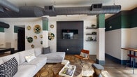 Located at 950 Riverside Dr in Chattanooga, Tennessee, this single-floor community amenity space blends industrial-chic aesthetics with vibrant, curated décor. Exposed ductwork runs across the ceilings, adding an urban edge that contrasts beautifully with white brick walls and bold teal and deep gray accent tones carried throughout the space.

The main lounge area is anchored by a large sectional sofa and an eye-catching dark wood panel wall featuring a mounted flat-screen television. Decorative woven wall art, floating shelves with greenery, and a geometric-patterned area rug over hardwood floors contribute to a warm, eclectic atmosphere. Natural wood coffee tables and a mix of seating, including an accent chair in rich burnt orange, create an inviting, layered environment.

A billiards room offers a full pool table set against more white brick and teal walls, with a wall-mounted cue rack and additional flat-screen television — ideal for social gatherings and recreation.

Adjacent areas open into a more expansive lounge with soaring double-height ceilings, wide-plank hardwood flooring, vivid blue seating arrangements, and wall sconces that illuminate framed artwork. Large sliding glass doors draw the eye outward to a pool area beyond, seamlessly connecting indoor comfort with outdoor leisure. The overall ambiance is modern, dynamic, and thoughtfully designed for community engagement.