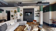 Located at 950 Riverside Dr in Chattanooga, Tennessee, this single-floor community amenity space blends industrial-chic aesthetics with vibrant, curated décor. Exposed ductwork runs across the ceilings, adding an urban edge that contrasts beautifully with white brick walls and bold teal and deep gray accent tones carried throughout the space.

The main lounge area is anchored by a large sectional sofa and an eye-catching dark wood panel wall featuring a mounted flat-screen television. Decorative woven wall art, floating shelves with greenery, and a geometric-patterned area rug over hardwood floors contribute to a warm, eclectic atmosphere. Natural wood coffee tables and a mix of seating, including an accent chair in rich burnt orange, create an inviting, layered environment.

A billiards room offers a full pool table set against more white brick and teal walls, with a wall-mounted cue rack and additional flat-screen television — ideal for social gatherings and recreation.

Adjacent areas open into a more expansive lounge with soaring double-height ceilings, wide-plank hardwood flooring, vivid blue seating arrangements, and wall sconces that illuminate framed artwork. Large sliding glass doors draw the eye outward to a pool area beyond, seamlessly connecting indoor comfort with outdoor leisure. The overall ambiance is modern, dynamic, and thoughtfully designed for community engagement.