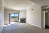 Located in Laguna Niguel, CA, this one-bedroom, one-bathroom residence offers a well-designed single-floor layout with thoughtful architectural details throughout. The spacious living room is a standout, featuring soaring vaulted ceilings with crown molding, a textured ceiling, plush wall-to-wall carpeting, and a tile-surround fireplace. Sliding glass doors open to a private balcony that captures sweeping outdoor views, flooding the room with natural light. The kitchen is efficiently laid out with white shaker cabinetry, dark countertops, stainless steel appliances including a refrigerator, range, microwave, and dishwasher, and hardwood-style flooring paired with a bright window overlooking greenery. The bedroom is generously proportioned with impressively tall ceilings, soft carpeting, a closet, and a window framing scenic treetop and hillside views. The bathroom features a single-sink vanity with a dark wood-tone countertop, a tub/shower combo with white surround, and a high window for natural light. A welcoming entryway with crown molding and recessed lighting completes this well-appointed Laguna Niguel residence.