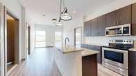 This well-appointed 2-bedroom, 2-bathroom unit at 383-389 Main St offers a thoughtfully designed single-floor layout with modern finishes throughout. The open-concept kitchen serves as the heart of the space, featuring rich dark-brown cabinetry, granite countertops, a central island with pendant lighting, white subway tile backsplash, and a full suite of stainless steel appliances. Light wood-style plank flooring flows seamlessly through the kitchen, living area, and bedrooms, contributing to a bright, cohesive aesthetic. The primary bedroom is generously sized, with large windows framing outdoor views, while the second bedroom also benefits from natural light and a sliding closet door. A balcony access point with floor-to-ceiling glass provides elevated outdoor views of the surrounding neighborhood. The two bathrooms are finished with clean, contemporary tile work — one featuring a soaking tub with subway tile surround, and the en-suite offering a glass-enclosed walk-in shower. Dark-toned vanities with white countertops are present in both bathrooms, complementing the unit's consistent design language. A dedicated closet adds practical storage to the layout.