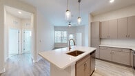 Located in West Melbourne, FL, this well-appointed 3-bedroom, 2-bathroom single-story home offers a thoughtfully designed layout with modern finishes throughout. The open-concept kitchen serves as the heart of the home, featuring a large center island with a white quartz countertop, a deep copper-toned undermount sink, gold-accented pendant lighting, and a full suite of stainless steel appliances. Taupe cabinetry with sleek hardware provides ample storage, while light wood-look flooring ties the kitchen seamlessly into the adjacent living area. The living room benefits from natural light through a large window and is finished with a ceiling fan. A central hallway connects the bedrooms, which are carpeted for comfort and feature multiple windows that invite natural light and outdoor views. The primary bedroom includes dedicated closet space with built-in wire shelving. The bathrooms are finished with modern grey cabinetry, quartz countertops, and wood-look flooring; one features a glass-enclosed walk-in shower with tile surround. Three closets throughout the home, including a walk-in, provide generous storage. The overall aesthetic is clean, bright, and contemporary, with neutral tones creating a welcoming and versatile living environment.