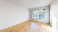 Located in Seattle's vibrant Roosevelt neighborhood, this one-bedroom, one-bathroom unit offers a thoughtfully organized single-floor layout. Light-toned hardwood flooring runs throughout the main living areas, reflecting natural light and creating a bright, airy atmosphere. The open combined living and dining area is anchored by a large picture window framing lush greenery outside, lending the space a calm, connected-to-nature feel. Recessed lighting complements the natural illumination throughout.

The compact kitchen is efficiently designed with stainless steel appliances, including a refrigerator and dishwasher, a single-basin sink, and upper cabinetry with frosted glass panels. A dedicated laundry area adds everyday convenience within the unit.

The bedroom features plush patterned carpeting, a window with natural light, and a closet with sliding doors for organized storage. The bathroom is clean and functional, appointed with large-format white subway tile surrounding a full soaking tub and shower, complemented by tile flooring and built-in shelving. A hallway connects the bedroom and bathroom, providing a clear and practical flow. The unit's neutral palette and clean finishes throughout create a cohesive, move-in-ready living environment.