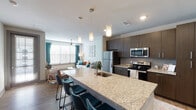 This thoughtfully designed one-bedroom, one-bathroom residence offers a functional and modern open-concept floor plan across a single level. The kitchen serves as the centerpiece of the living area, anchored by a generous granite-topped island with an undermount sink and seating for multiple guests. Dark espresso cabinetry extends floor to ceiling, providing ample storage, while a full suite of stainless steel appliances — including a refrigerator, electric range, and microwave — delivers a polished, contemporary aesthetic. Warm wood-style plank flooring flows seamlessly from the kitchen through to the living area, where oversized windows with blinds and teal accent drapes invite abundant natural light. A ceiling fan adds both comfort and style to the living room. The bedroom is a calm retreat, featuring plush carpeting, a ceiling fan, and a window framed by sheer curtains. The bathroom is well-equipped with both a soaking tub and a separate glass-enclosed shower, finished in clean white tile with granite accents. Throughout the residence, neutral wall tones, recessed lighting, and stylish pendant fixtures contribute to a cohesive, modern ambiance suitable for comfortable everyday living.