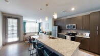 This thoughtfully designed one-bedroom, one-bathroom residence offers a functional and modern open-concept floor plan across a single level. The kitchen serves as the centerpiece of the living area, anchored by a generous granite-topped island with an undermount sink and seating for multiple guests. Dark espresso cabinetry extends floor to ceiling, providing ample storage, while a full suite of stainless steel appliances — including a refrigerator, electric range, and microwave — delivers a polished, contemporary aesthetic. Warm wood-style plank flooring flows seamlessly from the kitchen through to the living area, where oversized windows with blinds and teal accent drapes invite abundant natural light. A ceiling fan adds both comfort and style to the living room. The bedroom is a calm retreat, featuring plush carpeting, a ceiling fan, and a window framed by sheer curtains. The bathroom is well-equipped with both a soaking tub and a separate glass-enclosed shower, finished in clean white tile with granite accents. Throughout the residence, neutral wall tones, recessed lighting, and stylish pendant fixtures contribute to a cohesive, modern ambiance suitable for comfortable everyday living.
