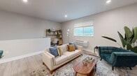 This two-floor unit offers a thoughtfully designed layout that maximizes functionality and comfort. The main living level, which comprises the majority of the floor area, is accessed via a carpeted staircase with a sleek white handrail, leading up to a bright and open living space. The combined kitchen and living room forms the heart of the unit, featuring light hardwood-style flooring that runs seamlessly throughout. The kitchen is well-equipped with white shaker-style cabinetry, granite countertops, stainless steel appliances including a refrigerator, range, and microwave, and a kitchen island with a deep sink. The living area is open and airy, with recessed lighting, a large window that allows ample natural light and outdoor views, and enough space to accommodate a comfortable seating arrangement alongside a dedicated workspace. The bathroom is finished with light hardwood-style flooring, white cabinetry with brushed hardware, a granite-topped vanity, a large mirror, and clean neutral walls that create a calm, spa-like atmosphere. The overall design palette is modern and cohesive, combining neutral tones, contemporary fixtures, and quality materials to deliver a polished and functional living environment.