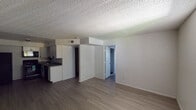 This single-floor unit offers a functional and straightforward layout designed for comfortable everyday living. The open-concept main area seamlessly connects the living space to the kitchen, creating a cohesive and practical floor plan. Laminate wood-style flooring runs consistently throughout the unit, providing a clean, uniform look that ties each room together.

The kitchen is positioned along one wall and is equipped with white cabinetry featuring modern hardware, dark countertops, a double-basin sink, a black electric range, an over-the-range microwave, and a dishwasher — offering a complete set of appliances for daily use. A structural soffit above the kitchen area adds architectural definition between the cooking and living zones.

The living area is generously proportioned, with neutral white walls and a textured popcorn ceiling that is consistent throughout the unit. A doorway leads from the main living space toward the private areas of the unit.

The bedrooms are well-sized, each featuring the same laminate flooring, white walls, and textured ceilings. Windows fitted with vertical blinds allow natural light to filter into the rooms while maintaining privacy. The overall ambiance of the unit is clean, neutral, and move-in ready, offering a blank canvas well-suited for a variety of interior styles.