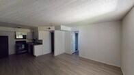 This single-floor unit offers a functional and straightforward layout designed for comfortable everyday living. The open-concept main area seamlessly connects the living space to the kitchen, creating a cohesive and practical floor plan. Laminate wood-style flooring runs consistently throughout the unit, providing a clean, uniform look that ties each room together.

The kitchen is positioned along one wall and is equipped with white cabinetry featuring modern hardware, dark countertops, a double-basin sink, a black electric range, an over-the-range microwave, and a dishwasher — offering a complete set of appliances for daily use. A structural soffit above the kitchen area adds architectural definition between the cooking and living zones.

The living area is generously proportioned, with neutral white walls and a textured popcorn ceiling that is consistent throughout the unit. A doorway leads from the main living space toward the private areas of the unit.

The bedrooms are well-sized, each featuring the same laminate flooring, white walls, and textured ceilings. Windows fitted with vertical blinds allow natural light to filter into the rooms while maintaining privacy. The overall ambiance of the unit is clean, neutral, and move-in ready, offering a blank canvas well-suited for a variety of interior styles.