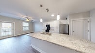 Located at 419 Donald Driver Way in Green Bay, WI, this well-appointed 2-bedroom, 2-bathroom unit offers a thoughtfully designed single-floor layout with modern finishes throughout. The open-concept kitchen serves as the centerpiece of the living space, featuring a large granite-topped island with a built-in sink, pendant lighting, crisp white shaker cabinets, and black appliances including a range, microwave, and stainless steel refrigerator. Light wood-style flooring flows throughout the kitchen and living areas, creating a clean and cohesive aesthetic. Both bedrooms are carpeted for comfort and include ceiling fans with lighting. The primary bedroom offers generous proportions and access to a walk-in closet fitted with wire shelving and hanging rods for ample storage. The two bathrooms are finished with white cabinetry, clean countertops, and light wood-style flooring. One bathroom features a tub-shower combo with subway tile surround and a large vanity mirror, while the second provides a functional shower space. Neutral wall tones and consistent trim work give the entire unit a fresh, move-in-ready feel. Windows in the living area and bedrooms allow for natural light, contributing to the bright and airy atmosphere throughout.