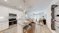 This well-appointed single-floor residence offers a thoughtfully designed open-concept layout that seamlessly connects the kitchen, dining, and living areas. The kitchen is a standout, featuring crisp white shaker cabinetry, granite countertops with a white-and-gray speckled finish, a classic subway tile backsplash, and a full suite of stainless steel appliances including a French door refrigerator, electric range, and built-in microwave. A generously sized island with an undermount sink provides seating for multiple guests, illuminated by elegant glass pendant lights overhead. Light wood-tone flooring flows throughout the main living areas, enhancing the bright and airy atmosphere. The living room is a comfortable, well-lit space anchored by large windows that invite natural light, complemented by a ceiling fan for year-round comfort. The primary bedroom offers a serene retreat with neutral tones and natural light from a large window. The primary bathroom is equipped with a dual-sink granite vanity, a glass-enclosed shower, and direct access to a walk-in closet with built-in shelving. Recessed lighting and a clean white palette throughout lend the entire space a modern, cohesive aesthetic.