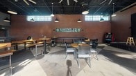 Located at 1102 3rd Ave in Nashville, TN, this single-floor commercial venue blends industrial design with Nashville's signature music culture. The interior showcases exposed brick walls, a black-painted open ceiling with visible ductwork and structural elements, and polished concrete floors that carry throughout the space. Large pendant lights and overhead fans provide both illumination and airflow across the expansive main floor.

A prominent feature is the substantial concrete bar, built atop a stone base, offering generous counter space for service. Behind the bar, stainless steel refrigeration units and a full back bar setup support high-volume operations. The "Open Stage" branded area signals a dedicated performance zone, complete with draped curtains and a stage backdrop — a fitting nod to Nashville's live music heritage.

The venue's standout architectural element is its oversized glass garage doors, which retract fully to merge the interior with an outdoor patio area. The patio features seating with city views, seamlessly extending the venue's capacity. Clerestory windows along the upper brick walls draw in abundant natural light, brightening the dining and lounge areas furnished with wood-top tables and modern metal chairs. A "Voluntler" branded sign further anchors the space in its local Nashville identity.