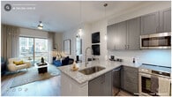 This 2-bedroom, 2-bathroom residence offers a well-planned open-concept layout filled with contemporary finishes and cohesive design details. The kitchen is a standout feature, showcasing grey shaker cabinetry extending to the ceiling, granite countertops, a herringbone tile backsplash, and a full suite of stainless steel appliances including a French door refrigerator, range, microwave, and dishwasher. A peninsula with pendant lighting and bar seating connects the kitchen seamlessly to the living area, which is bathed in natural light from large sliding glass doors opening to a private balcony with courtyard views. Wood-style plank flooring runs throughout the main living areas, lending warmth and continuity. The primary bedroom features rich, deep-toned walls and ample space, while the secondary bedroom offers its own distinct palette and comfortable proportions. Both bedrooms are served by well-appointed bathrooms; one features a granite-topped vanity with grey cabinetry, and the other includes a glass-enclosed walk-in shower with marble-style tile surround. A dedicated hallway with closet storage and an in-unit laundry area add practical convenience. The overall ambiance is modern and refined, balancing functional living with elevated aesthetic details throughout.