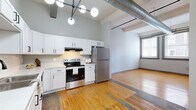 Located at 1004 W Baltimore in Kansas City, MO, this one-bedroom, one-bathroom loft blends industrial character with modern updates. The open layout is unified by warm hardwood flooring that runs throughout, complemented by soaring ceilings, exposed spiral ductwork, and structural beams that lend an authentic urban loft aesthetic.

The kitchen is a standout feature, outfitted with crisp white shaker cabinets, light countertops, a black matte faucet, and a full suite of stainless steel appliances including a refrigerator, electric range, and dishwasher. A contemporary globe chandelier and pendant lighting add a stylish finishing touch overhead.

The spacious bedroom offers a comfortable footprint with natural light streaming through double windows fitted with blinds. A ceiling fan provides year-round comfort, and large sliding wood-panel doors lead to a closet. Exposed ductwork continues the industrial theme carried throughout the unit.

The bathroom is clean and functional, featuring a white vanity with under-cabinet storage, a framed mirror with vanity lighting above, and a shower with curtain enclosure, all set on the same warm hardwood flooring found throughout the space.

Additional living areas provide flexible, open space ideal for a living or dining arrangement, making this loft a well-rounded urban residence in the heart of Kansas City.