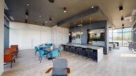 Located at 2109 S Wabash Ave in Chicago's South Loop neighborhood, this contemporary amenity lounge is a thoughtfully designed communal space that blends industrial aesthetics with upscale finishes. The open floor plan is anchored by an expansive bar island topped with sleek stone countertops, lined with navy and gold bar stools and illuminated by a striking cluster of globe and dome pendant lights in brushed gold. Behind the bar, textured tile walls and built-in cabinetry create a sophisticated backdrop, complete with a large mounted display screen.

Raw concrete accent walls punctuate the interior, adding an industrial edge that contrasts beautifully with the light wood-plank flooring. A generous dining and lounge area features rich wood tables surrounded by teal upholstered chairs, offering flexible seating arrangements. Floor-to-ceiling glass walls and sliding doors on one side flood the space with natural light while framing panoramic views of the surrounding Chicago skyline and neighborhood rooftops. These doors open directly onto a spacious outdoor terrace furnished with seating, turf, and high-top tables.

A dedicated game zone features wood-paneled ceilings, a teal bench, arcade machines, and casual seating, adding a playful element to the space. A refined wet bar alcove with mosaic tile detailing and framed mirror niches rounds out the amenities, creating a well-appointed, multi-functional gathering space.