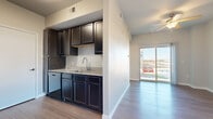This efficiently designed 1-bedroom, 1-bathroom unit offers a thoughtful single-floor layout encompassing a living room, kitchen, bedroom, bathroom, and hallway. The living area is bright and welcoming, featuring smooth hardwood-style flooring, neutral gray walls, a ceiling fan with light fixture, and a sliding glass door that fills the space with natural light and provides direct outdoor views. The kitchen is a functional galley-style space outfitted with rich dark espresso cabinetry, granite-patterned countertops, a stainless steel sink, and black appliances including a refrigerator, range, microwave, and dishwasher. It opens conveniently toward the living area, creating an accessible flow between spaces. The bedroom is carpeted for comfort, features a ceiling fan, a window with exterior views, and includes a closet for storage. The bathroom is neatly finished with dark cabinetry, a granite-topped vanity with an undermount sink, large-format tile surround in the tub/shower combination, and hardwood-style flooring. Throughout the unit, consistent design elements — including white trim, neutral paint tones, and coordinated dark cabinetry — create a cohesive and modern aesthetic.