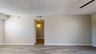 This single-floor unit offers a clean, modern aesthetic throughout, with consistent wood-look plank flooring and a neutral color palette that creates a cohesive and inviting atmosphere. The open living area is generously sized, featuring a textured ceiling, ceiling fan with light fixture, and smooth white walls that allow for flexible furniture arrangements. A wall sconce-lit passageway connects the living space to the bedroom corridor, adding a warm transitional touch.

The galley-style kitchen is thoughtfully designed with crisp white shaker cabinetry, classic white subway tile backsplash, and gray countertops. Stainless steel appliances — including a refrigerator, electric range, over-the-range microwave, and dishwasher — provide a polished, functional finish. A window with horizontal blinds allows natural light to brighten the space.

The bedroom is a comfortable, well-lit room with its own ceiling fan, a window overlooking the outdoors, and matching wood-look flooring. The bathroom is finished in a clean, all-white style featuring a soaking tub with built-in shower surround, recessed shelving niches, and classic fixtures. Overall, the unit presents a refreshed, move-in-ready environment with thoughtful details throughout.