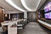 Located at 882 Juniper St NE in Atlanta's Midtown neighborhood, this single-floor space presents a refined, hospitality-forward design with a cohesive aesthetic defined by warm walnut wood paneling, patterned carpet with flowing linear motifs, and carefully layered lighting throughout.

The main gathering area serves as the focal point of the space, anchored by a dramatic built-in media wall featuring multiple flat-screen displays arranged around a central large-format screen. Flanking architectural elements include illuminated vertical panels and curved walnut millwork, lending the wall a polished, broadcast-ready character. A marble-topped table and curated seating arrangements—including a plush tan sofa, a velvet lounge chair, and mid-century-style accent seating—create an inviting and functional environment.

Floor-to-ceiling charcoal drapery lines the perimeter, softening the interior ambiance while providing visual continuity. A sweeping curved architectural arch visible in the overhead view adds a sculptural quality to the open plan layout.

The kitchenette area features rich walnut cabinetry, dark granite countertops, a mosaic tile backsplash, and a stainless steel sink, providing practical support for events or hospitality functions. Throughout the space, recessed lighting and strategic accent illumination enhance the sophisticated, contemporary atmosphere.