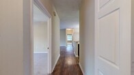 Located at 565 Saint Johns Avenue Southwest in Atlanta, Georgia, this single-story, three-bedroom, two-bathroom home offers a practical and comfortable layout across a well-proportioned floor plan. The interior is unified by rich, dark hardwood-style flooring throughout the main living areas and hallways, complemented by plush carpeting in each of the three bedrooms.

The living room is a standout space, featuring large windows that flood the area with natural light and offer views of the surrounding greenery. A decorative column accent adds architectural character to the room. The adjacent kitchen is well-appointed with white cabinetry, a tile backsplash, light countertops with a peninsula, a black electric range, and a dishwasher — all centered around hardwood-style flooring.

The bedrooms are generously sized, with the primary bedroom offering ample space, a ceiling fan, and a large window with outdoor views. All bedrooms include dedicated closets with wire shelving for storage. The two bathrooms each feature a full tub-and-shower combination with clean white surrounds. A dedicated laundry area with hookups adds everyday convenience. A central hallway connects all areas of the home efficiently, completing this well-organized single-level residence.