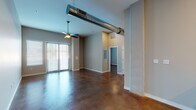 This single-floor loft-style unit delivers an industrial-modern aesthetic defined by rich, polished stained concrete floors that run throughout the entire space. The expansive open-concept living area commands attention with soaring ceilings and a bold exposed cylindrical HVAC duct running overhead, adding an authentic industrial character. Ceiling fans are featured throughout, enhancing airflow and comfort across every room. Large sliding glass doors with vertical blinds in the living area invite natural light and provide outdoor access.

The kitchen is thoughtfully designed with white shaker cabinetry, light quartz countertops, a subway tile backsplash, and a full suite of stainless steel appliances including a refrigerator, range, over-the-range microwave, and dishwasher. A peninsula counter offers additional workspace and casual dining potential.

Two well-proportioned bedrooms each feature ceiling fans, natural light from windows with blinds, and double closets. The in-unit laundry area with a stacked washer and dryer adds everyday convenience. The bathroom is finished with a white vanity topped with quartz countertops, a framed mirror, and a tub-shower combination enclosed by sliding glass doors with brushed nickel hardware — completing this well-appointed, urban-inspired residence.