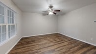 Located at 2001 Slayden St in Brownwood, Texas, this 2-bedroom, 2-bathroom unit offers a practical and well-organized single-floor layout. The combined living, dining, and kitchen area forms an open-concept hub at the heart of the unit. Rich, dark wood-look plank flooring flows through the main living spaces, anchored by a front entry door and a window that brings in natural light. The galley-style kitchen is efficiently designed with warm oak cabinetry extending to the upper walls, a full suite of white appliances including a refrigerator and electric range, a double-basin sink, and a tile backsplash that complements the neutral palette throughout. Both bedrooms are carpeted for comfort and are equipped with ceiling fans. Each bedroom benefits from direct access to a bathroom — featuring wood-toned vanities with granite-style countertops — and generously sized closets. With four closets total across the unit, storage is a notable strength of this floor plan. The bathrooms include tub-shower combinations with clean white tile surrounds. Neutral wall tones and consistent finishes throughout give the unit a cohesive, move-in-ready appearance well-suited for everyday living.
