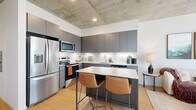 Located in the heart of downtown Phoenix at 440 E Van Buren St, this one-bedroom, one-bathroom residence blends industrial design with contemporary finishes across a thoughtfully laid-out single floor. Exposed concrete ceilings and structural columns serve as defining architectural elements throughout, lending an urban loft aesthetic that is both striking and cohesive.

The open-concept kitchen is outfitted with matte gray flat-front cabinetry, stainless steel appliances, a subway tile backsplash with under-cabinet lighting, and a peninsula with a quartz countertop and bar seating — ideal for casual dining or entertaining. Light wood flooring flows seamlessly into the living room, where floor-to-ceiling windows frame city views and fill the space with abundant natural light. A prominent concrete column anchors the living area, adding to the space's industrial character.

The bedroom offers a serene retreat with continued concrete ceiling details, a sliding barn door, and access to a dedicated closet. The bathroom features large-format tile flooring, a glass-enclosed walk-in shower with vertically laid white tile, and a modern vanity with clean, minimal finishes.

Throughout the unit, white walls provide a neutral backdrop that balances the rawness of the concrete and highlights the warm wood tones, creating a refined yet edgy urban living environment.