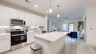 This well-appointed single-story residence offers three bedrooms and three bathrooms across a thoughtfully designed floor plan. The open-concept kitchen and living area serves as the heart of the home, featuring bright white shaker-style cabinetry, a subway tile backsplash, stainless steel appliances including a range, microwave, refrigerator, and dishwasher, and a large center island with a white quartz countertop illuminated by pendant lighting above. Light wood-style flooring flows seamlessly throughout the entire space, contributing to a cohesive and airy aesthetic. The living area receives generous natural light through a glass door and adjacent window, with a ceiling fan adding to the comfort of the space. Each bedroom is well-proportioned, with the primary suite featuring a dedicated walk-in closet equipped with wire shelving and a private en-suite bathroom complete with a dual-sink vanity, white cabinetry, and a glass-enclosed shower. Additional bathrooms include a tub-shower combination. The secondary bedrooms offer closet storage and access to natural light through windows with blinds. A hallway connects the private quarters to the main living areas, and the overall color palette of whites and soft neutrals creates a clean, modern ambiance throughout.