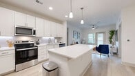 This well-appointed single-story residence offers three bedrooms and three bathrooms across a thoughtfully designed floor plan. The open-concept kitchen and living area serves as the heart of the home, featuring bright white shaker-style cabinetry, a subway tile backsplash, stainless steel appliances including a range, microwave, refrigerator, and dishwasher, and a large center island with a white quartz countertop illuminated by pendant lighting above. Light wood-style flooring flows seamlessly throughout the entire space, contributing to a cohesive and airy aesthetic. The living area receives generous natural light through a glass door and adjacent window, with a ceiling fan adding to the comfort of the space. Each bedroom is well-proportioned, with the primary suite featuring a dedicated walk-in closet equipped with wire shelving and a private en-suite bathroom complete with a dual-sink vanity, white cabinetry, and a glass-enclosed shower. Additional bathrooms include a tub-shower combination. The secondary bedrooms offer closet storage and access to natural light through windows with blinds. A hallway connects the private quarters to the main living areas, and the overall color palette of whites and soft neutrals creates a clean, modern ambiance throughout.