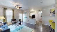 This single-story residence offers a smartly designed layout encompassing one bedroom, two bathrooms, a combined dining room, kitchen, and living area, plus a closet and hallway. The open-concept living and dining area is anchored by hardwood-style flooring, crown molding, and a ceiling fan, creating a bright and welcoming atmosphere. Large windows allow natural light to fill the space, complemented by neutral gray walls that provide a versatile backdrop. The kitchen features white cabinetry, a gray subway tile backsplash, light countertops, black appliances, and a central window above the sink — all connected to the main living area via a peninsula counter. The dining area accommodates a round table beneath a pendant light, with a decorative mirror adding depth to the room. The bedroom is comfortably sized, carpeted, and includes a ceiling fan and multiple windows with blinds offering natural light. Two bathrooms serve the residence, one featuring a full soaking tub with shower combination and extended vanity with ample cabinet storage. The hallway connects the rooms efficiently, maintaining a clean and organized flow throughout the entire space.