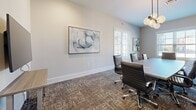 Located in Columbia, Tennessee, this professional conference room offers a refined and functional environment designed for productive meetings. The space centers around a large rectangular conference table surrounded by sleek, high-back leather executive chairs, providing ample seating for a full team. Neutral-toned walls in soft gray and warm white create a clean, contemporary backdrop throughout the room.

A wall-mounted flat-screen display is positioned at one end of the room atop a slim console table, making it well-suited for presentations. On the opposite end, a set of vertical acoustic panels in muted tones of cream, taupe, and mauve contribute both visual interest and sound management. A tall potted fiddle-leaf fig plant adds a touch of warmth and organic texture to the space.

Multiple windows fitted with white plantation shutters line the walls, inviting abundant natural light while maintaining privacy. The windows offer views of the surrounding Columbia streetscape. Framed abstract artwork in cool blue and gray tones is thoughtfully displayed across the walls, reinforcing the polished aesthetic.

Patterned commercial carpet in earthy brown and gray tones grounds the room while adding durability. Recessed and pendant lighting complement the natural light, ensuring a well-illuminated setting. Overall, the space exudes a professional yet approachable atmosphere ideal for collaboration.