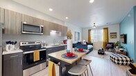 This single-floor studio-style unit is thoughtfully designed to maximize functionality within a compact, open-concept layout. Light wood-look flooring runs throughout, creating a cohesive and airy feel across all areas of the space.

The kitchen is a standout feature, offering a full suite of stainless steel appliances including a refrigerator, electric range, over-the-range microwave, and dishwasher. Two-tone cabinetry — with upper cabinets in a light wood-grain finish and lower cabinets in a deep charcoal tone — adds visual depth, while recessed lighting illuminates the workspace. A freestanding kitchen island with a butcher block top and bar seating provides a casual dining and prep area.

The open living area flows seamlessly from the kitchen, offering flexible space for lounging and sleeping. A ceiling fan with a light fixture enhances comfort, while windows dressed with horizontal blinds and warm gold curtains allow for natural light and outdoor views. The bathroom features a full soaking tub and shower combination, a single-sink vanity with wood-accented cabinetry, and clean, neutral finishes. An in-unit stacked washer and dryer is also included, adding everyday convenience. The overall ambiance is modern, bright, and efficiently arranged.