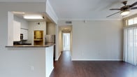 This 1-bedroom, 1-bathroom residence, designated as unit A3, offers a thoughtfully designed single-floor layout that maximizes both comfort and functionality. The open-concept living area is anchored by rich, dark hardwood-style flooring that runs throughout the space, creating a warm and cohesive aesthetic. Crown molding along the ceilings adds a refined architectural touch, while crisp white walls and neutral tones contribute to a bright, clean atmosphere.

The kitchen features a raised breakfast bar with a dark granite-style countertop, providing a natural divide between the cooking and living areas. Stainless steel appliances, including a refrigerator, are complemented by under-cabinet lighting that adds both practicality and ambiance. A utility area is visible within the kitchen space, offering added convenience.

A hallway leads from the main living area toward the bedroom and bathroom, with recessed lighting guiding the way. The entryway, visible at the end of the corridor, is framed by a bright door that invites natural light into the space. Ceiling vents throughout ensure efficient climate control. Overall, the unit presents a clean, modern living environment well-suited for those seeking a straightforward and functional residential space.