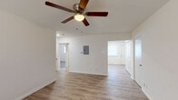 This single-story residence presents a clean, functional layout finished with consistent wood-look laminate flooring throughout. The open living area is anchored by a five-blade ceiling fan with integrated lighting and features a centrally mounted electrical panel, with connecting doorways leading to adjacent rooms and a hallway beyond. Crisp white walls and neutral tones establish a bright, airy atmosphere across the entire space.

The bedrooms each include ceiling fans with lighting and windows fitted with horizontal blinds, allowing for controlled natural light. The rooms offer adequate space for furnishings and are finished with the same continuous flooring found throughout the residence.

The kitchen is well-appointed with dark espresso-toned cabinetry extending to the ceiling for generous storage, white countertops, a corner sink, and a full suite of appliances including a stainless steel electric range, over-the-range microwave, dishwasher, and refrigerator. A window above the dining area brings in natural light, enhancing the functional workspace.

The bathroom features a full tub-shower combination with white subway tile surround and built-in shelving, a vanity with a large mirror, and clean white fixtures throughout. Overall, the space presents a well-maintained, move-in-ready interior with practical finishes and a cohesive design.