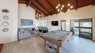 Located at 10343 San Diego Mission Rd, this single-story community clubhouse offers a thoughtfully designed gathering space that blends architectural character with modern amenities. The heart of the facility is a dramatic open-concept recreation and lounge area defined by soaring vaulted ceilings clad in rich warm wood beams, creating an inviting, airy atmosphere. Light-toned hardwood-style flooring runs throughout, complementing the white walls adorned with colorful contemporary artwork. Contemporary globe and geometric chandeliers provide warm, ambient lighting throughout the space.

The game area features a full-size pool table with a rustic wood frame and a shuffleboard table, offering ample room for social activity. Adjacent to the game area, a comfortable lounge zone is furnished with a sectional sofa, tufted armchairs in deep navy blue, a round coffee table, and a patterned area rug — all centered beneath a statement chandelier. A wall-mounted flat-screen television anchors the entertainment area.

A dedicated meeting or conference room provides a more intimate setting, equipped with a large wall-mounted display, a rectangular table, and cognac leather chairs, accented by natural wood wall art and an abstract painting.

The covered outdoor patio extends the usable space, featuring wicker lounge chairs with teal cushions overlooking lush tropical greenery — ideal for relaxed conversation or quiet retreat.