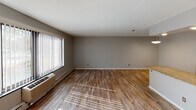 This single-floor unit offers a clean, functional layout designed for comfortable everyday living. The spacious living area is finished with light hardwood-style flooring and neutral gray walls, creating a bright and welcoming atmosphere. Large windows fitted with vertical blinds allow generous natural light to filter across the space, while baseboard heating and a wall-mounted HVAC unit ensure year-round climate control.

The galley-style kitchen is thoughtfully designed with rich dark-stained cabinetry, granite countertops, a stainless steel sink, and a full suite of appliances including a refrigerator, electric range, microwave, and dishwasher. A pass-through counter connects the kitchen to the living area, enhancing the open feel of the space.

Two bedrooms are carpeted in a neutral tone and each feature a window with vertical blinds and baseboard heating, providing a quiet and comfortable retreat. The full bathroom is finished with a granite-topped dark wood vanity, a wide mirror with overhead lighting, tile wainscoting, and classic mosaic tile flooring, complemented by a bathtub and toilet. The overall design is cohesive and move-in ready, with consistent finishes throughout.