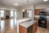 This single-floor residence is designed with an open, functional layout that seamlessly connects the main living areas. The kitchen serves as a central hub, featuring warm medium-toned wood cabinetry, granite-look countertops, and a full suite of black appliances including a range, microwave, refrigerator, and dishwasher. A peninsula with pendant lighting overhead provides additional prep space and separates the kitchen from the open living area, which is finished with light hardwood-style flooring that extends throughout the main areas of the unit.

The living room is generously proportioned, with a ceiling fan overhead and access to a sliding glass door that brings in natural light. An adjacent area, also with hardwood-style flooring and a window, offers additional flexible living space.

The bedrooms are carpeted for comfort and feature neutral walls with warm wood trim accents. One carpeted bedroom includes a ceiling fan and sliding glass door access. Two bathrooms serve the unit — one featuring a full tub-shower combination with tile flooring and wood cabinetry, and a second with a vanity, toilet, and tile flooring. The overall design is clean and cohesive, with consistent trim work and neutral tones throughout.