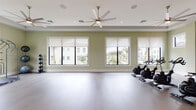 Located at 15616 SW 127th Ave in Miami, FL, this single-floor fitness and recreation facility is thoughtfully designed to support a wide range of health and wellness activities. The main gym area is expansive, featuring plush carpeting, multiple ceiling fans, and an array of professional-grade TKO strength machines, a heavy punching bag, and cardio equipment including treadmills and cable machines. Full-length mirrors line one wall, enhancing the sense of openness throughout the workout space.

A dedicated spin studio adjoins the main gym, outfitted with stationary cycling bikes and a wall-mounted display screen. Light hardwood-style flooring, large windows with roller shades, and a tray ceiling with a ceiling fan create a bright, airy atmosphere ideal for cycling classes. A separate strength and flexibility room provides space for free weights, medicine balls, stability equipment, and a functional training cage, all set against soft green walls and natural light.

The facility also includes a vibrant children's playroom featuring a bold nature-inspired wall mural, a colorful striped area rug, child-sized furniture, an easel, and a play tent, offering a stimulating environment for younger visitors. Dedicated men's and women's restrooms are conveniently accessible. Throughout the facility, soft sage-green walls and recessed lighting contribute to a clean, welcoming ambiance.