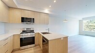 Located at 2900 Tillicum Road in Victoria, BC, this well-appointed one-bedroom, one-bathroom unit offers a thoughtfully designed layout across a single floor. The open-concept living and kitchen area sets a modern tone, featuring light wood cabinetry, stainless steel appliances including a gas range, microwave, and refrigerator, and a sleek peninsula with a white quartz countertop and undermount sink. Warm hardwood flooring flows throughout the main living areas, complementing the clean, neutral palette of the walls and recessed lighting overhead. The bedroom is a bright, serene retreat, benefiting from a large picture window that frames views of mature evergreen trees and connects the interior to the natural surroundings outside. A baseboard heater ensures year-round comfort. The bathroom is finished with contemporary details, including a light wood vanity with a white countertop, stone-look tile flooring, and a sliding glass shower enclosure. In-suite laundry adds a practical convenience to the unit. The overall ambiance is clean, modern, and efficient — an ideal space for those seeking functional urban living in a well-designed setting.