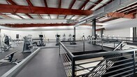 This state-of-the-art exercise facility spans an impressive 6,610 square feet on a single floor, designed to cater to a wide range of fitness needs. The space features a striking industrial-modern aesthetic, characterized by exposed ceiling structures with prominent red beams and white ductwork, creating a sense of openness and height.

The facility is thoughtfully divided into distinct workout zones. A spacious cardio area houses an array of treadmills and elliptical machines, while a separate section is dedicated to strength training, equipped with various weight machines and free weights. The layout promotes easy navigation, with yellow guide lines on the floor directing traffic flow.

Large windows flood the space with natural light, offering views of the surrounding area and contributing to an energizing atmosphere. The facility also incorporates specialized areas, including a space for stability ball exercises and what appears to be a track or circuit training area.

Safety and cleanliness are evident in the design, with ample space between equipment and modern finishes that are easy to maintain. The industrial elements are softened by the use of neutral tones and the inclusion of green accents, such as exercise balls and flooring in certain areas.

This well-equipped and thoughtfully designed space at 1735 Tribe Dr, Biloxi, MS, provides a comprehensive and inviting environment for fitness enthusiasts of all levels.
