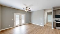 Located at 65 Patriot Dr in Bardstown, Kentucky, this well-appointed 2-bedroom, 2-bathroom residence offers a thoughtfully designed single-floor layout. The open-concept kitchen and living area serves as the heart of the home, featuring warm hardwood-style flooring throughout. The kitchen is outfitted with rich, gray-toned shaker cabinetry, granite countertops, and a full suite of stainless steel appliances including a side-by-side refrigerator with ice and water dispenser, electric range with over-the-range microwave, and dishwasher. The living room is bright and airy, anchored by a ceiling fan with light fixture and French doors that open to an outdoor balcony, filling the space with natural light. Both bedrooms are carpeted for comfort, with the primary bedroom featuring a generous walk-in closet equipped with wire shelving for ample storage. The second bedroom includes a standard closet and its own ceiling fan. Two full bathrooms serve the residence, each with hardwood-style flooring; one features a dark-toned vanity with a wide countertop, undermount sink, and a tub/shower combination. A dedicated laundry area and a connecting hallway complete the functional floor plan of this comfortable Bardstown home.